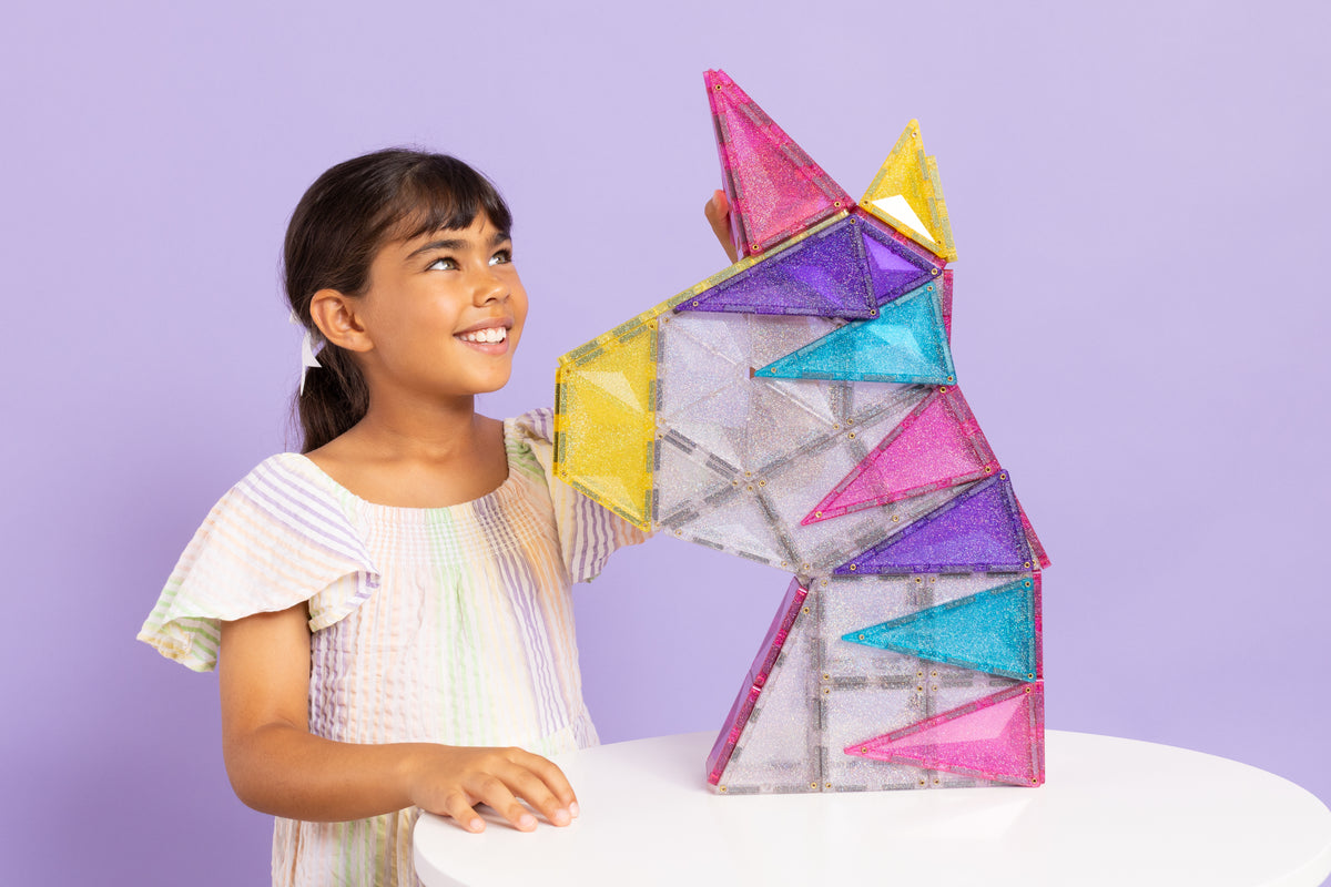 Meisje bouwt kleurrijke unicorn met Connetix Glitter Unicorn Pack 56pc magnetische tegels op witte tafel
