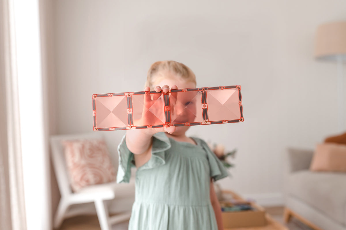 Kind toont roze Connetix Pastel Rectangle Pack 24pc magnetisch speelgoed in lichte woonkamer