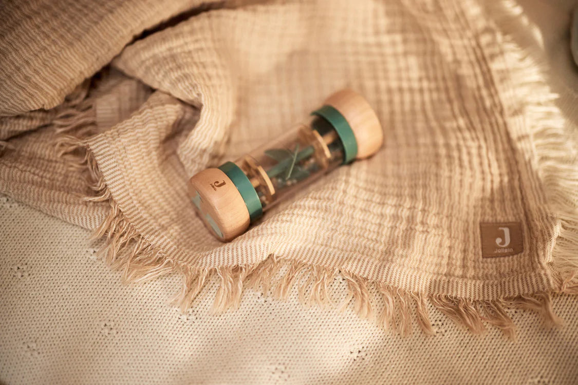 Educatief peuter speelgoed van Jollein: houten rammelaar met blauwe tinten, liggend op een beige hydrofiele doek.