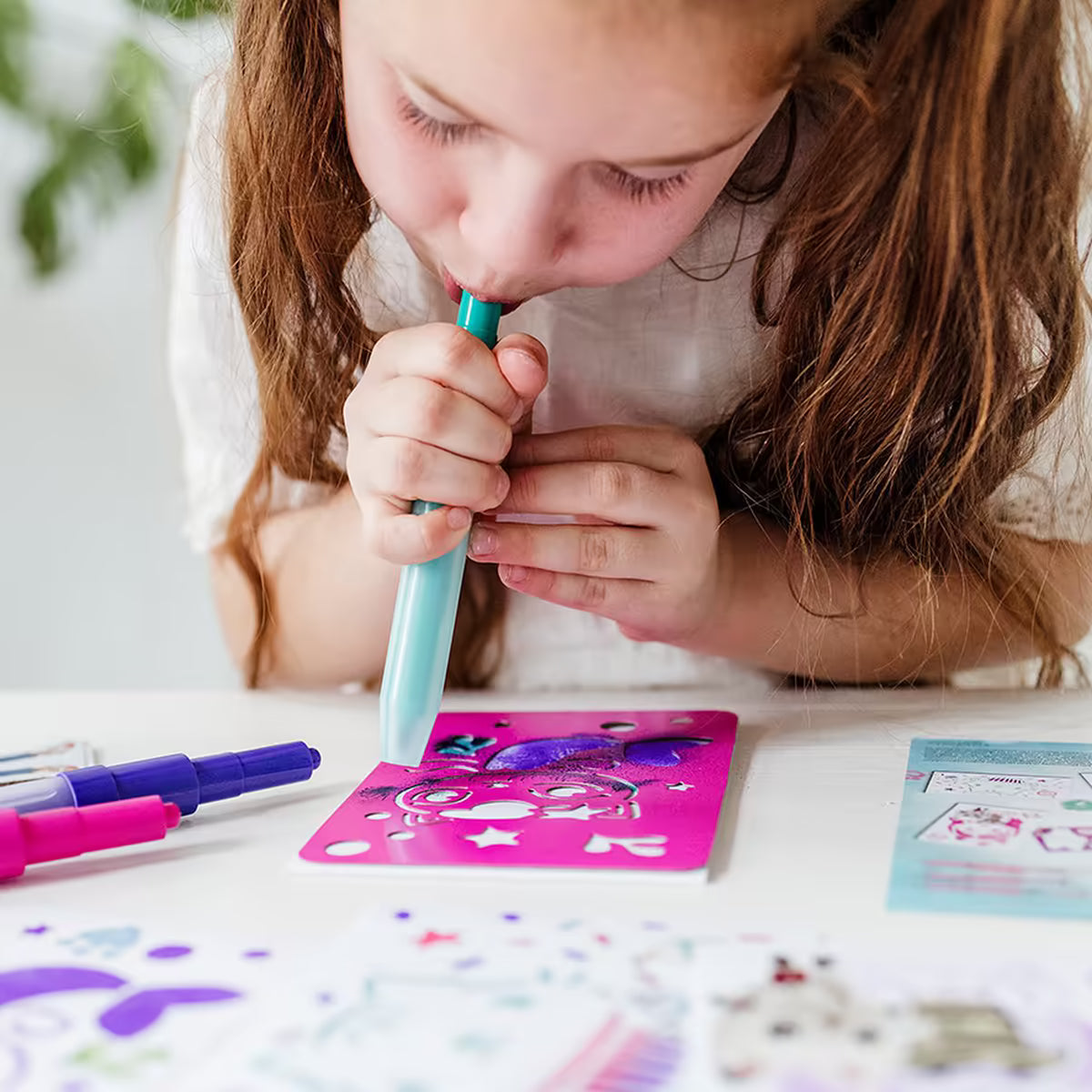 Meisje spuit blauwe spraypen op stencil uit Gabby’s Dollhouse creatieve set, creatieve knutsel ideeën voor peuters.