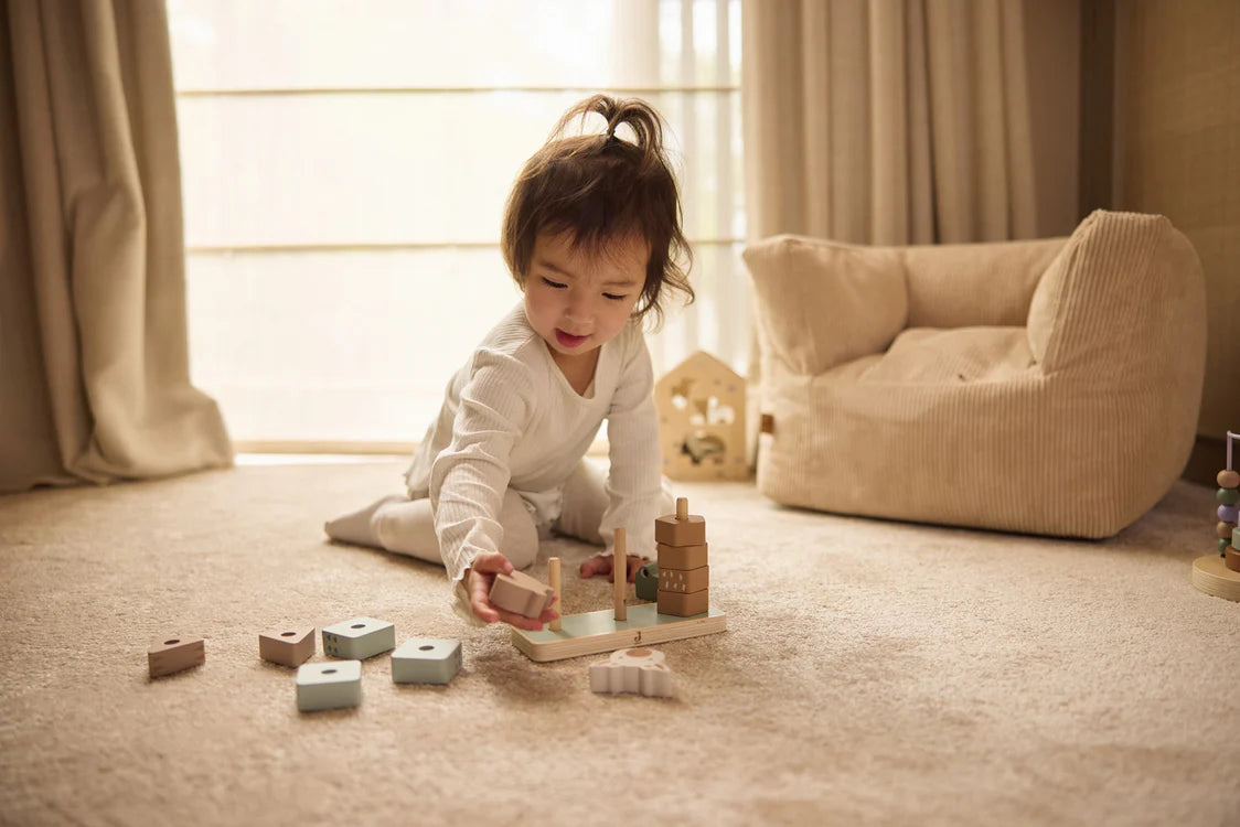 Peuter speelt geconcentreerd op vloer met houten stapeltoren van Jollein, perfect als educatief Montessori speelgoed.