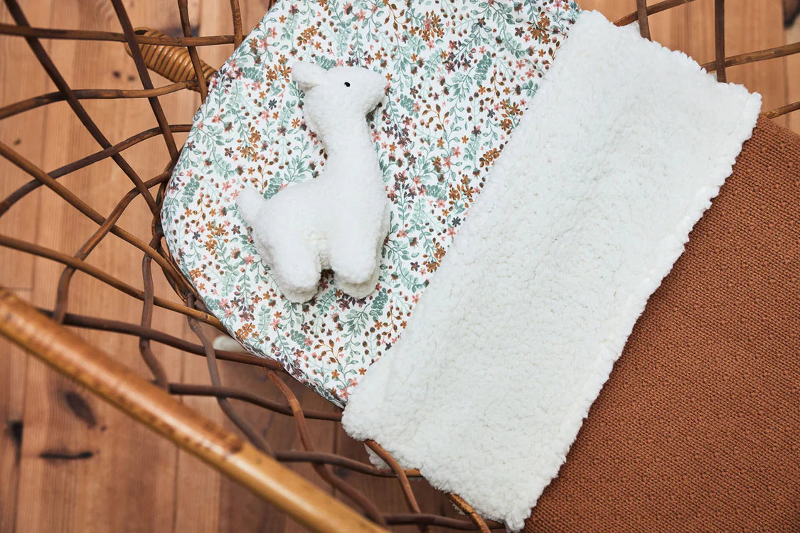 Jollein knuffel lama off-white op bloemendekentje in een rotan stoel als decoratief kraamcadeau.