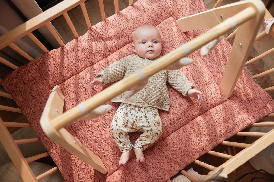 Baby ligt in houten wieg onder Jollein babygym met maan speeltjes in beige kleur, ideaal baby speelgoed.