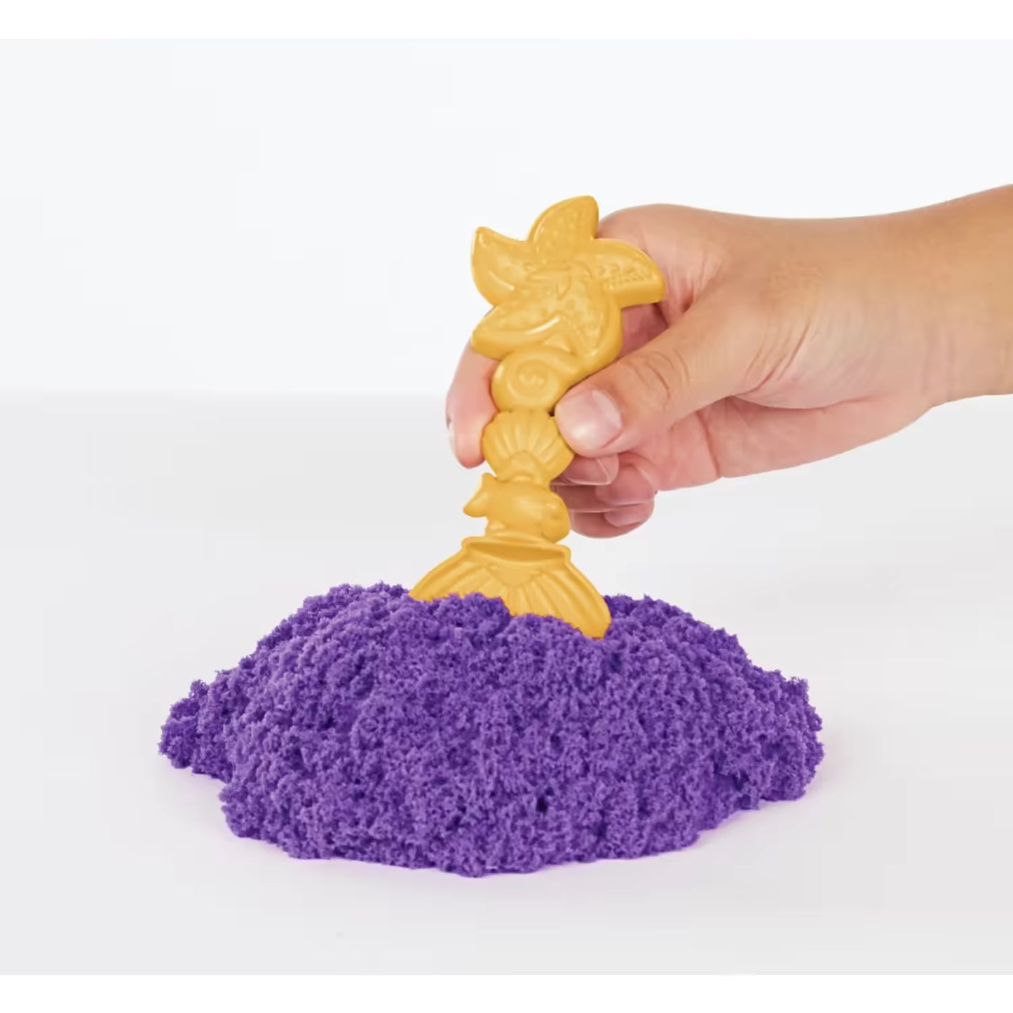 Hand met gouden mermaid-vormige tool in paars kinetisch zand, ideaal sensorisch speelgoed voor kinderen.