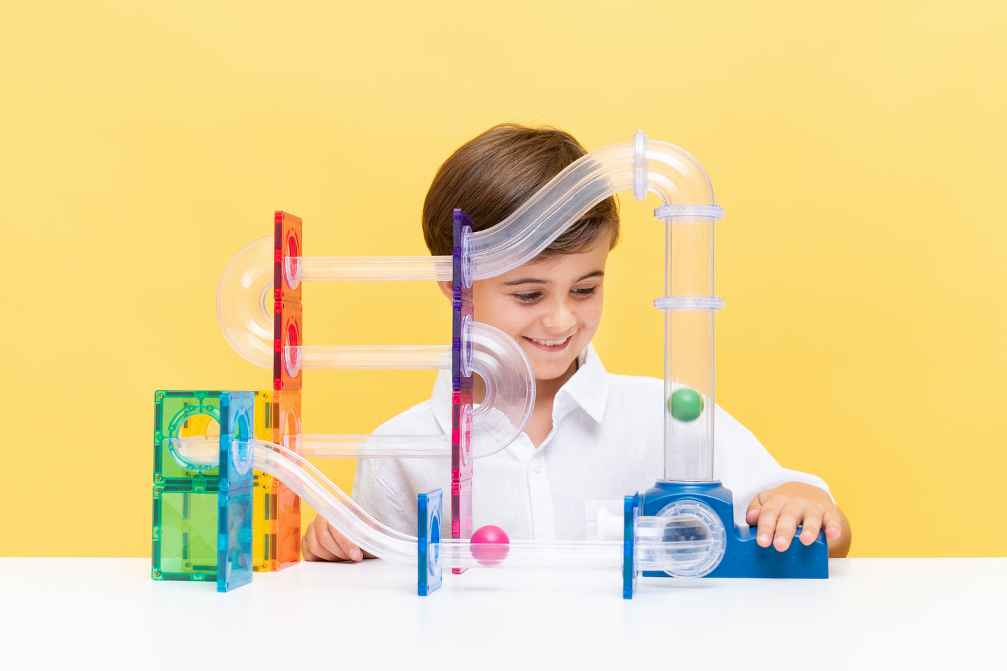 Meisje speelt met Connetix ball run launcher pack, magnetische tegels knikkerbaan gele achtergrond