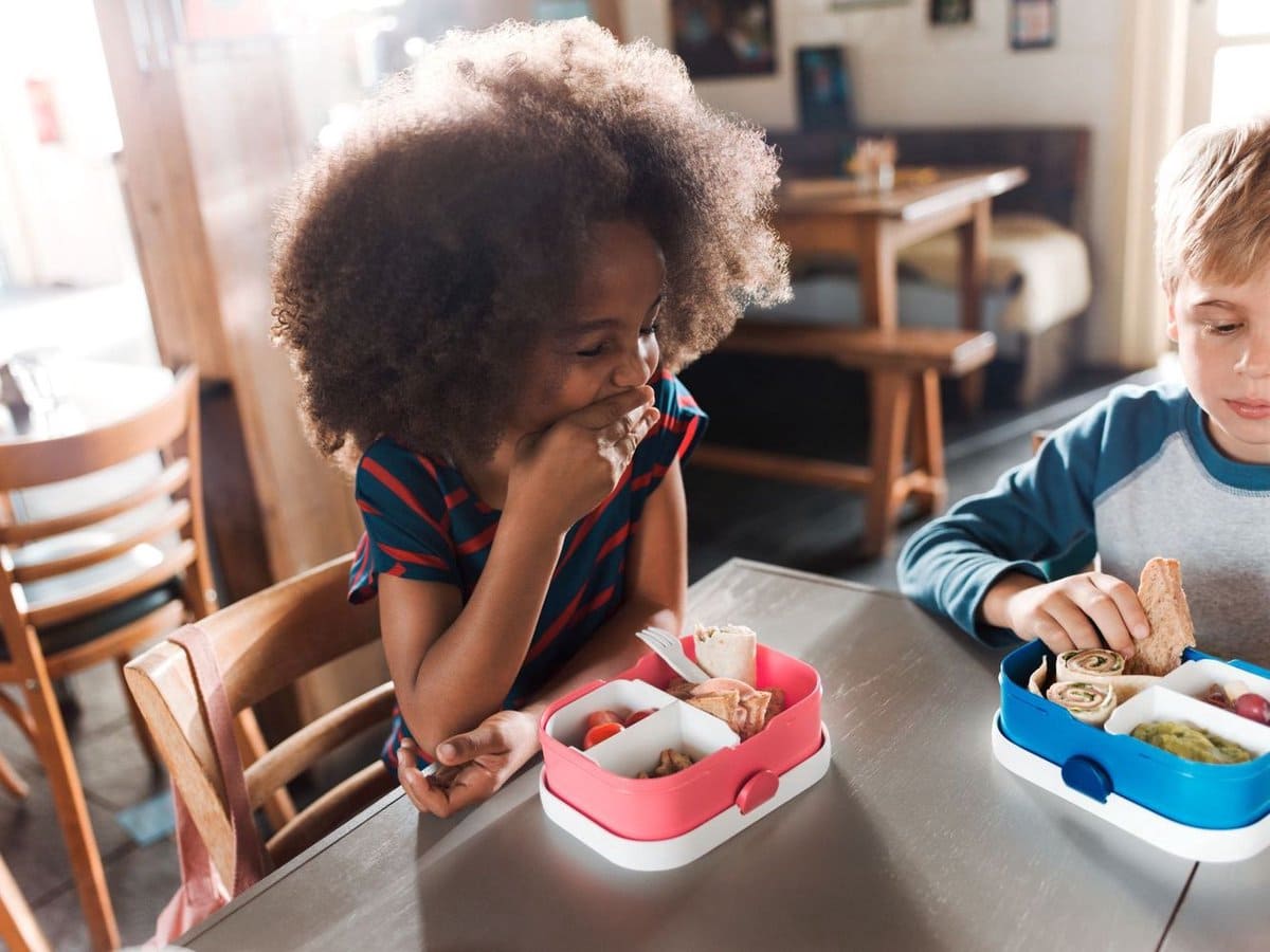 Twee kinderen eten samen aan tafel met Mepal lunchboxen in roze en blauw, gezellig en praktisch voor schoollunch