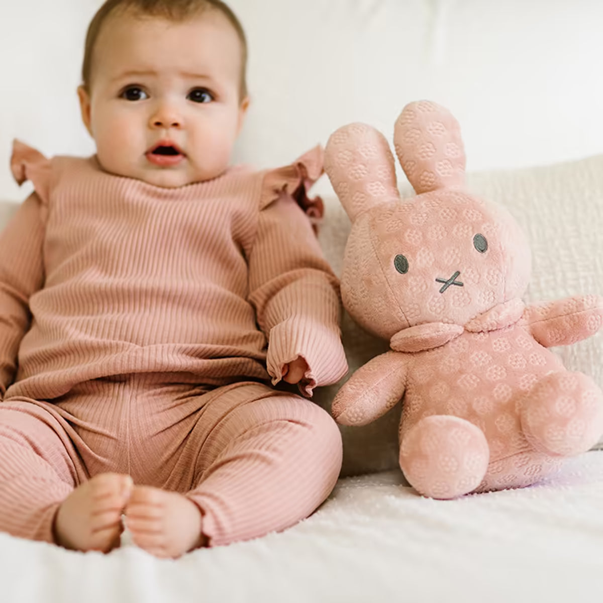 Baby in roze outfit naast zachte Nijntje Knuffel, ideaal babycadeau en kraamcadeau.