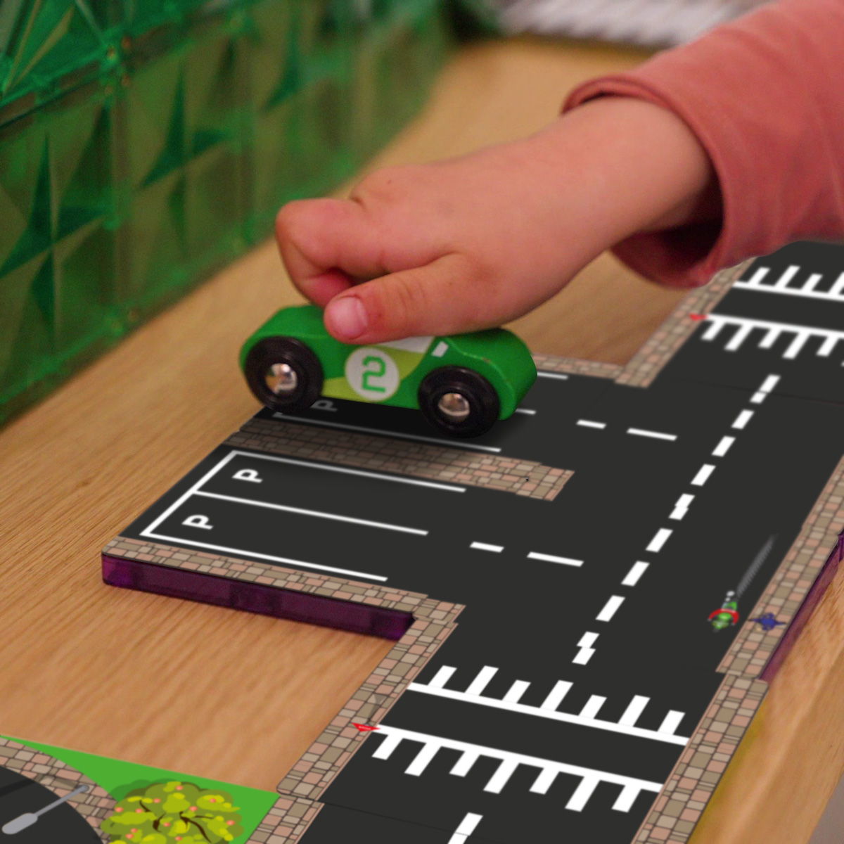 Close-up kinderhand duwt groene Coblo auto over magneet wegtegel met parkeerplaats