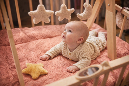 Baby doet tummy time onder houten babygym en kijkt naar hangende ster- en maanspeeltjes op een zacht speelkleed.