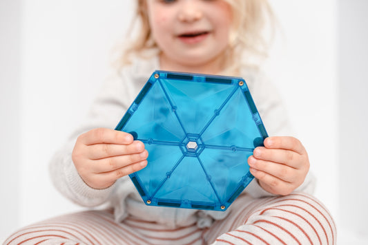 Kleuter houdt blauwe Connetix magnetische tegel met zichtbare klinknagels vast, veilig magnetisch speelgoed voor de klas