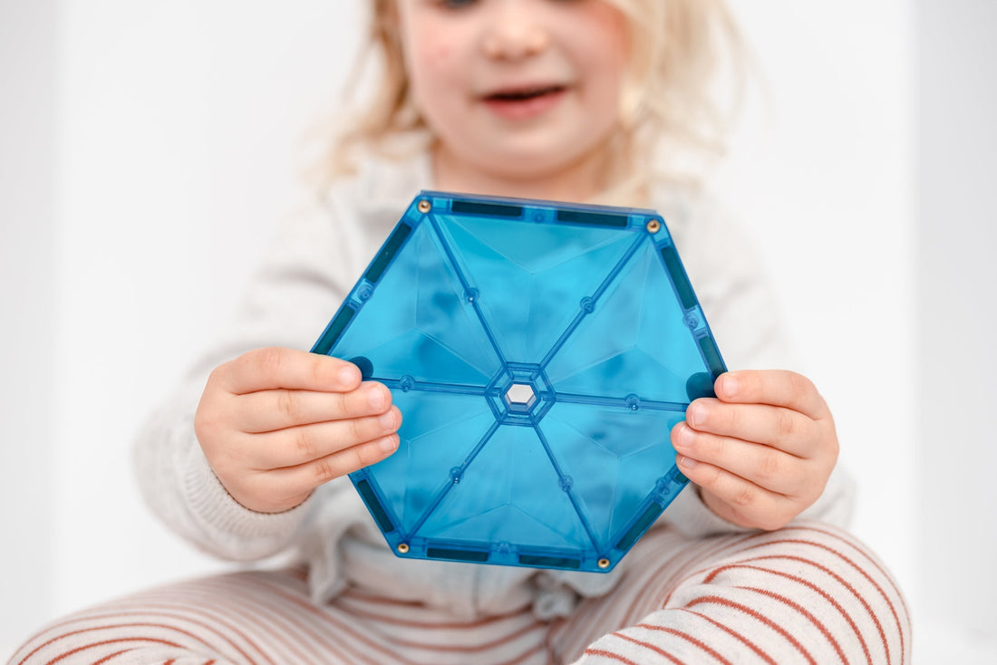 Kleuter houdt blauwe Connetix magnetische tegel met zichtbare klinknagels vast, veilig magnetisch speelgoed voor de klas