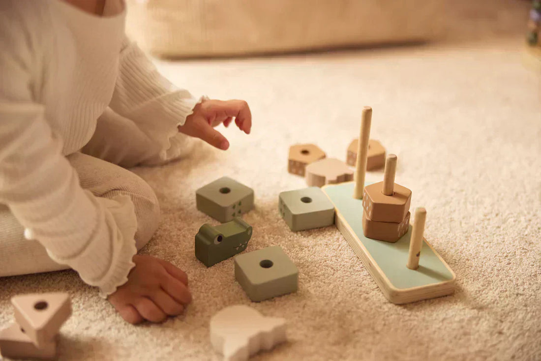 baby speelt met houten montessori speelgoed op vloerkleed met stapeltoren.