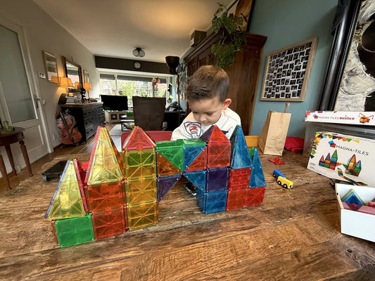 Kind bouwt kleurrijk kasteel met Magna Tiles op tafel, magnetisch speelgoed voor creatief en ruimtelijk spel.