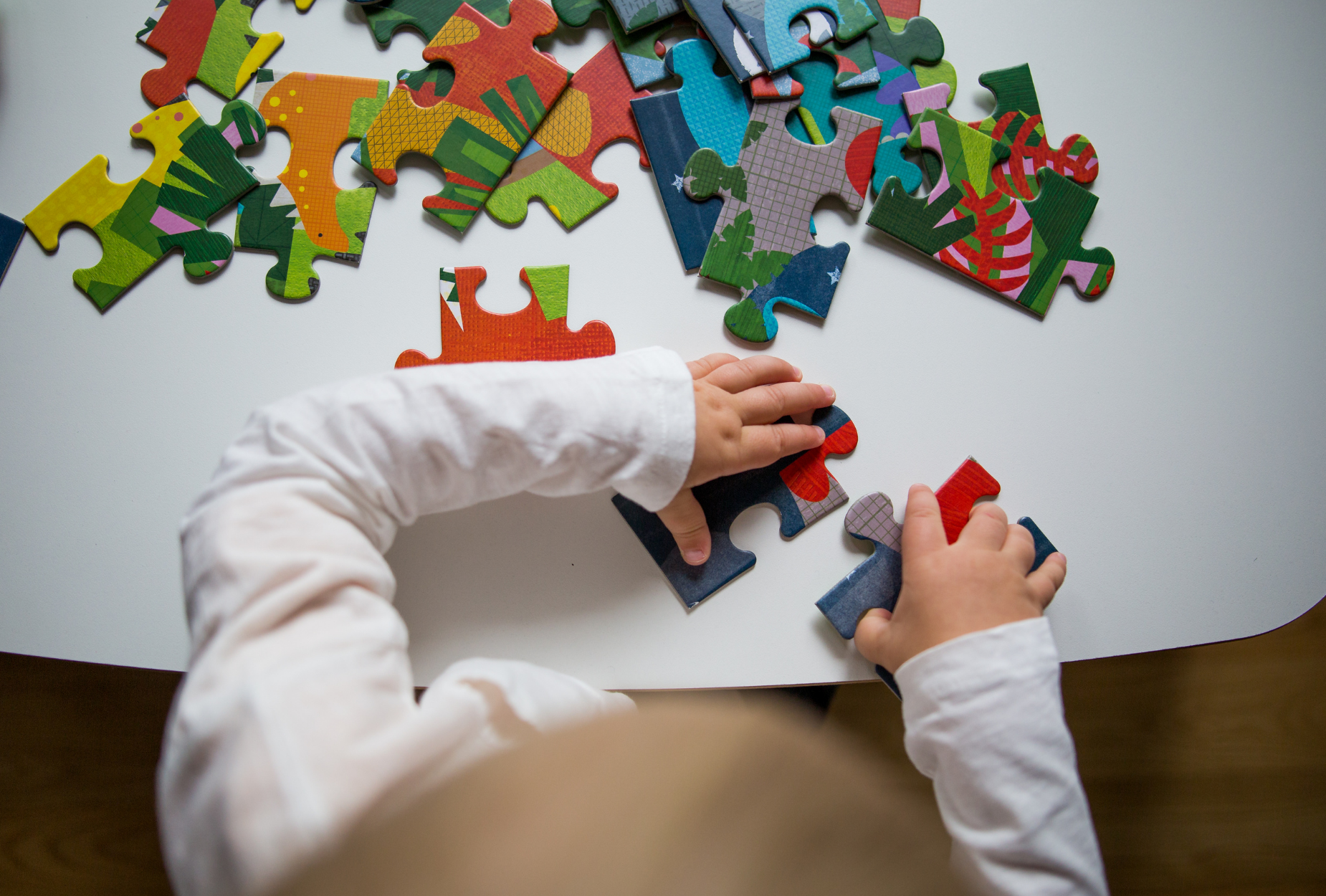 Kind legt grote kleurrijke puzzelstukjes op tafel, spelenderwijs leren en ontdekken met Ravensburger puzzels voor kinderen.