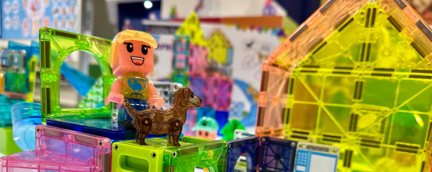 Kind speelt met een hondfiguur en bouwt een kleurrijk huis van magnetische Magna Tiles op een poef in een gezellige woonkamer.