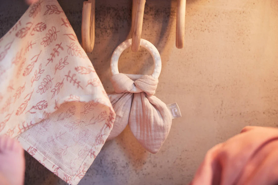 Jollein Bijtring Bunny Ears Nougat hangt aan houten haakje naast doek, sfeervol als baby cadeau decoratie.