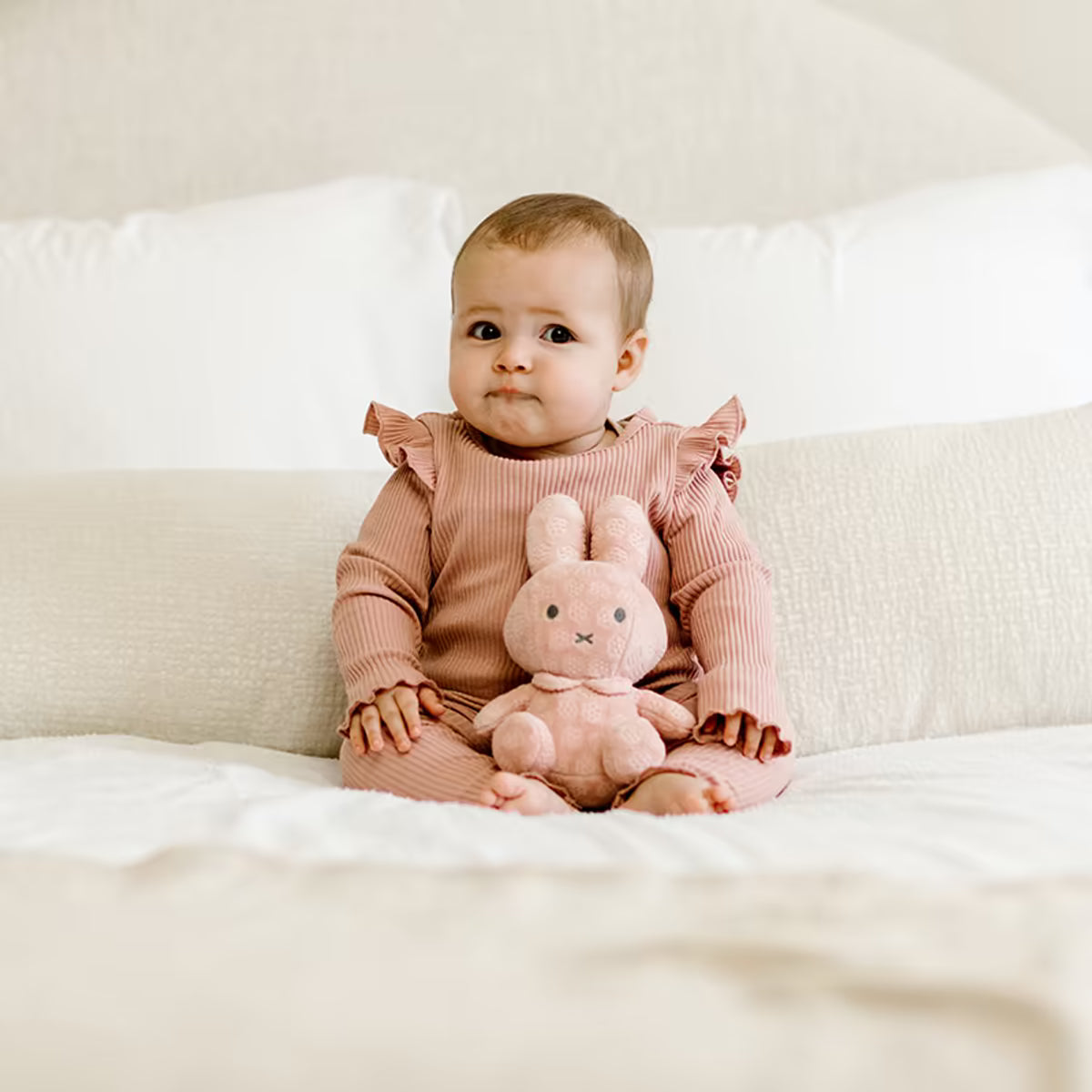 Baby zit op bed met roze Nijntje knuffel Pink Flower 20cm, een perfect kraamcadeau en baby cadeau.