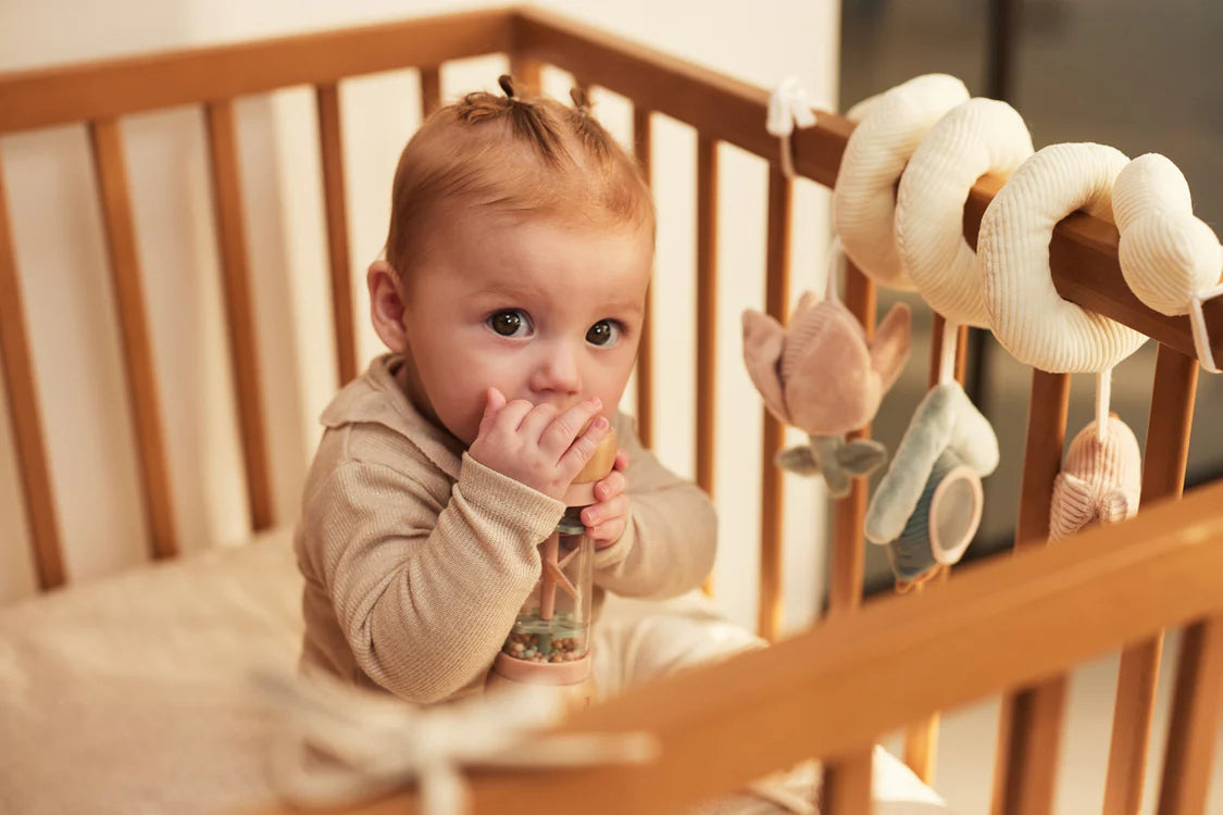 Baby speelt met roze houten rammelaar van Jollein in ledikant, uit de Lovely Birds collectie, veilig peuter speelgoed.