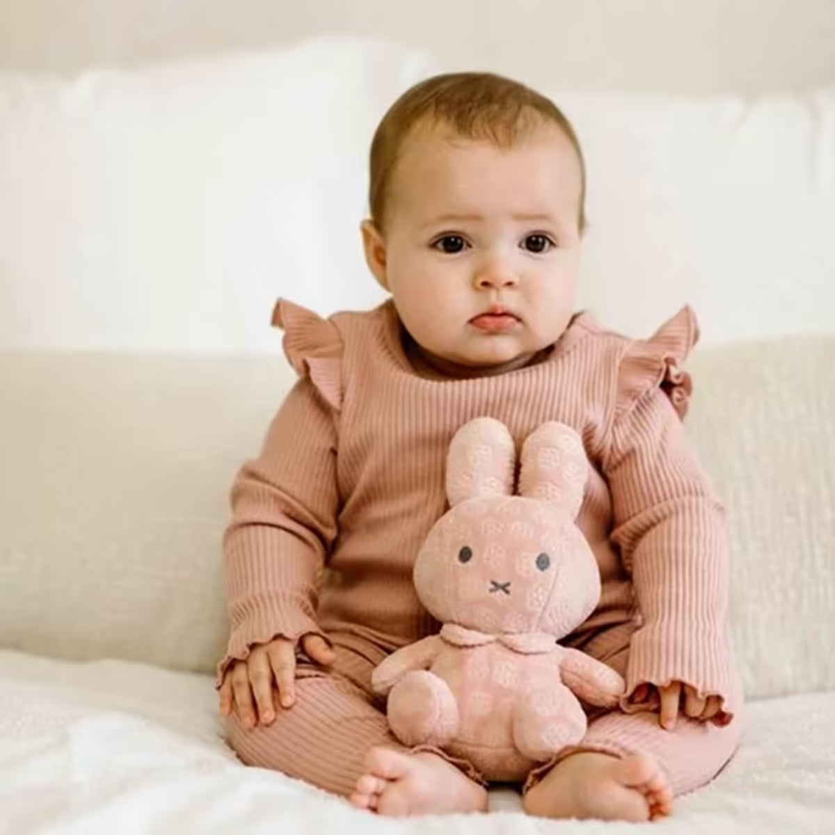 Baby zit met roze Nijntje knuffel Pink Flower 20cm op bed, ideaal kraamcadeau en zachte knuffel.