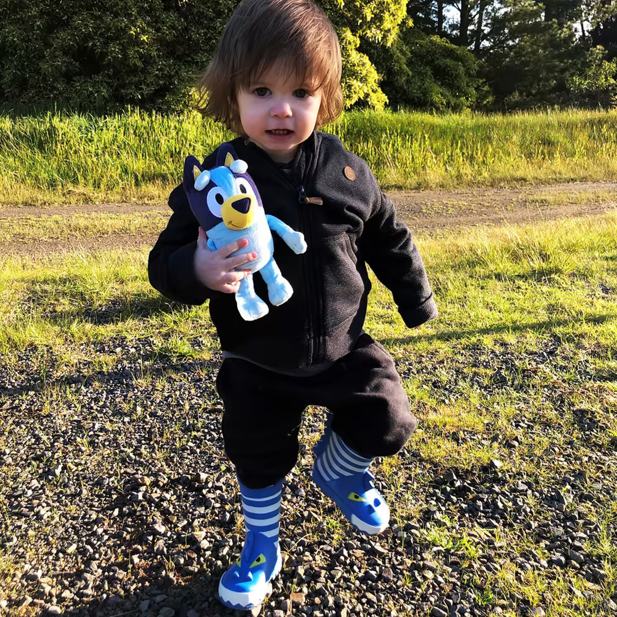 Peuter speelt buiten met Bluey pluche knuffel, een vrolijk speelvriendje en veilig sensorisch speelgoed.