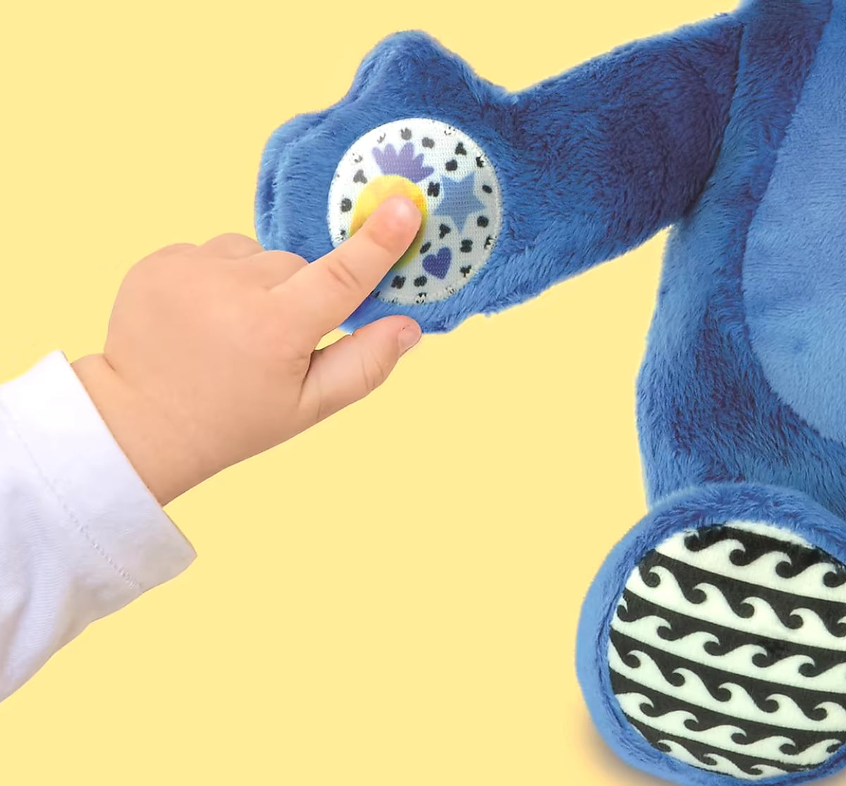 Detail van hand met interactieve knop op Clementoni Stitch Knuffel Musical Activity, stimulerend sensorisch peuter speelgoed.