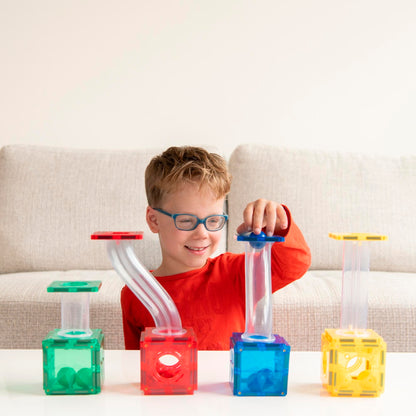 Jongen met bril bouwt coblo knikkerbaan voorbeeld met vier kleurrijke magnetische tegels en buizen