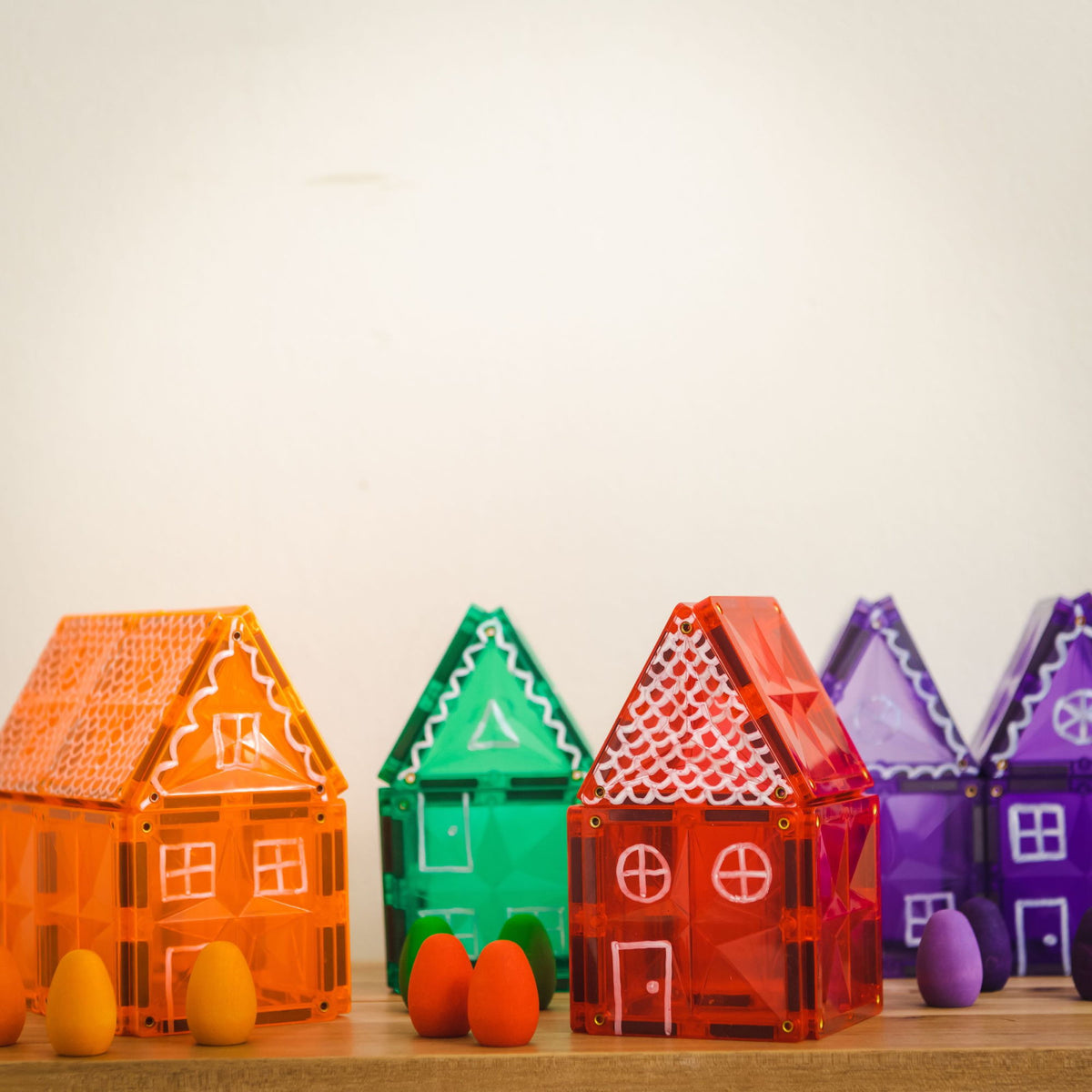 Coblo magneten huisjes in oranje, groen, rood en paars met witte decoratie op houten ondergrond