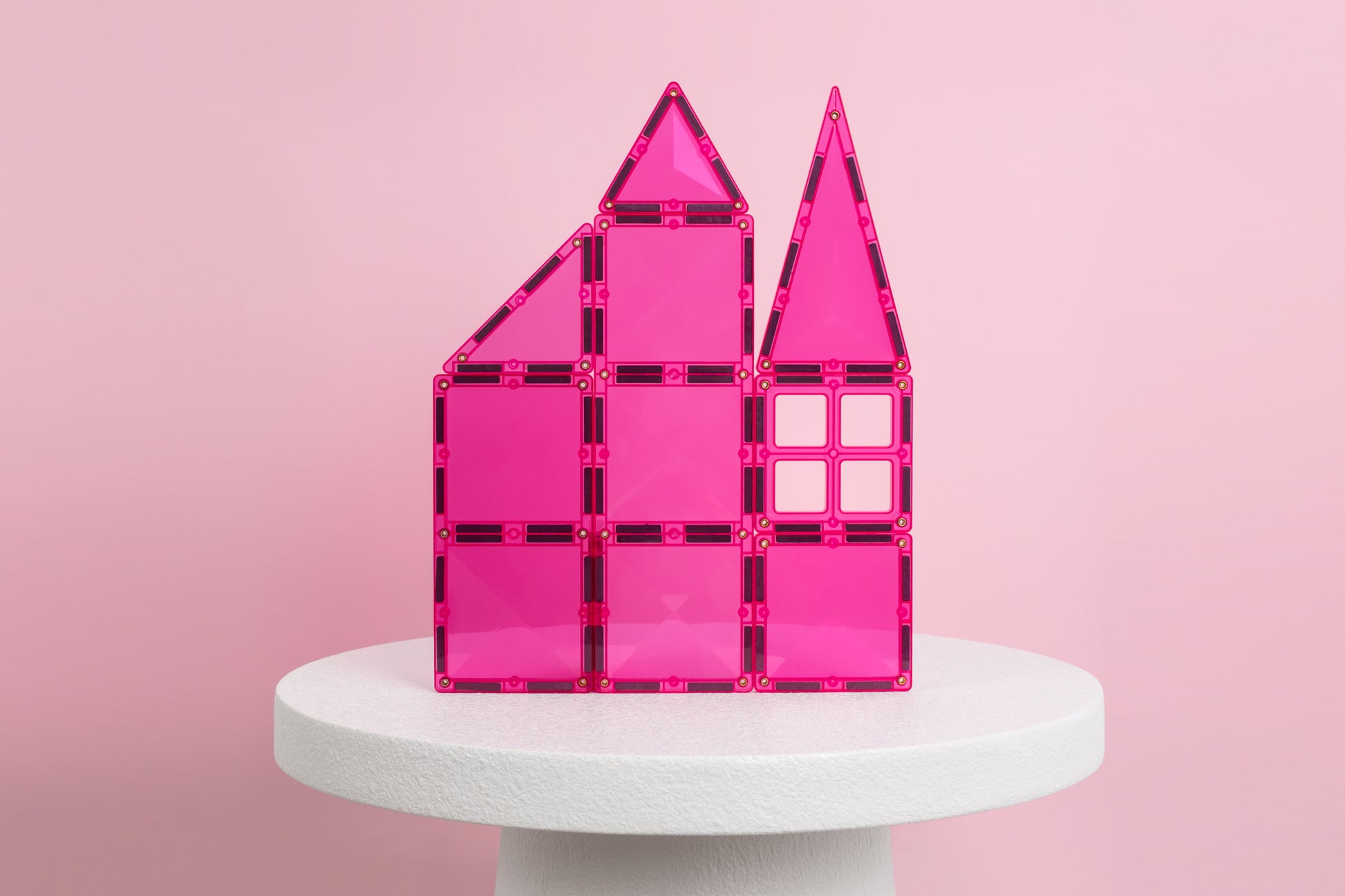 Connetix Charity Pack Pink 20pc: roze magnetische tegels bouwen kasteel met torens op witte sokkel, roze achtergrond.