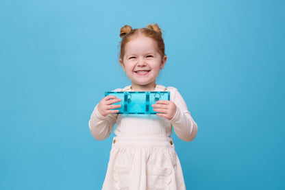 Connetix Charity Pack Teal 20pc – blij meisje toont lachend teal rechthoekige magnetische tegel op blauwe achtergrond.