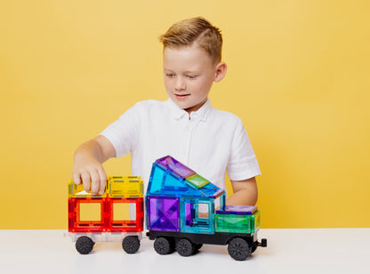 Kind speelt met Connetix magneet speelgoed trein in regenboogkleuren - creatief bouwen op gele achtergrond