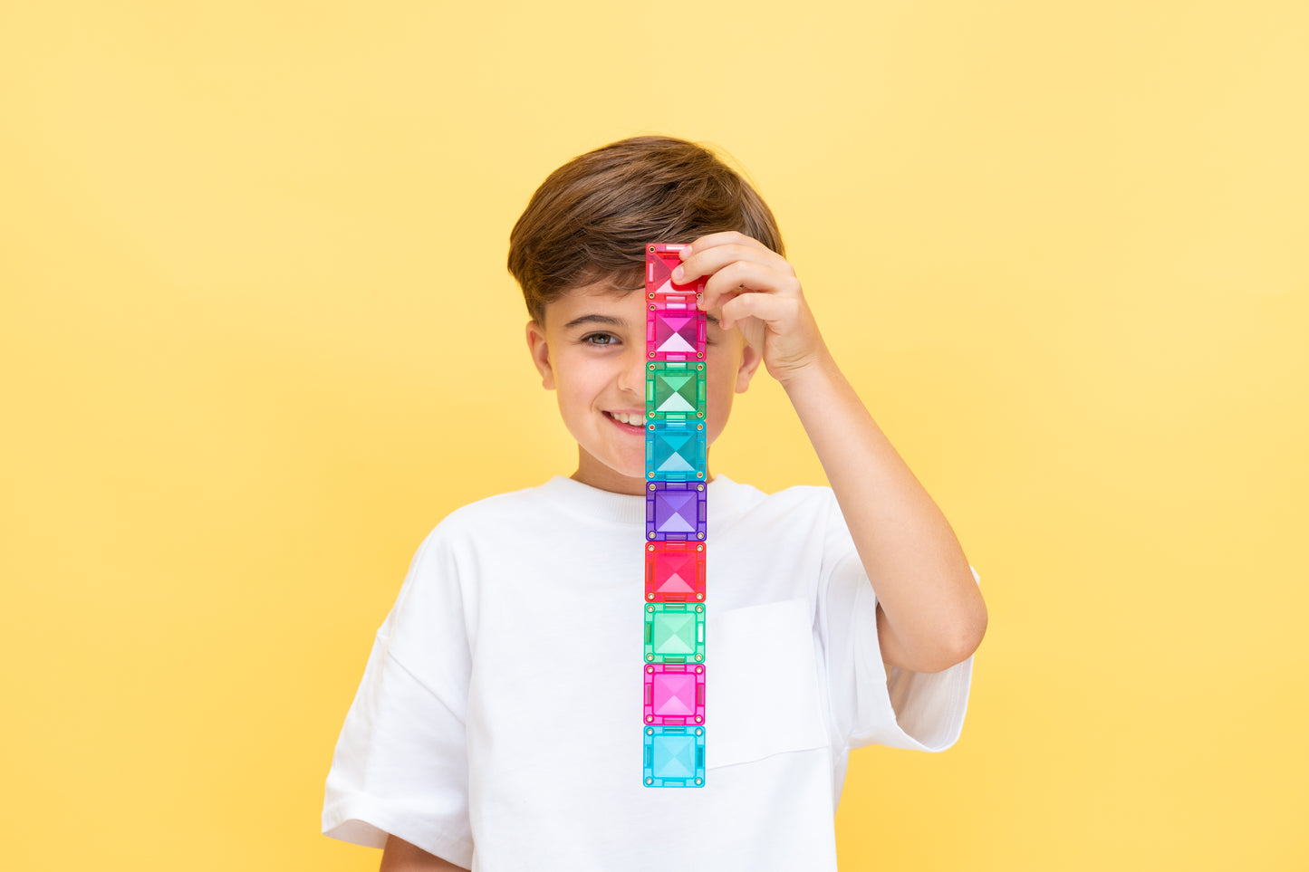 Connetix travel mini pack jongen houdt toren van kleurrijke magnetische tegels op gele achtergrond