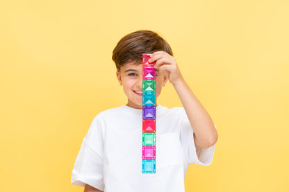 Connetix travel mini pack jongen houdt toren van kleurrijke magnetische tegels op gele achtergrond