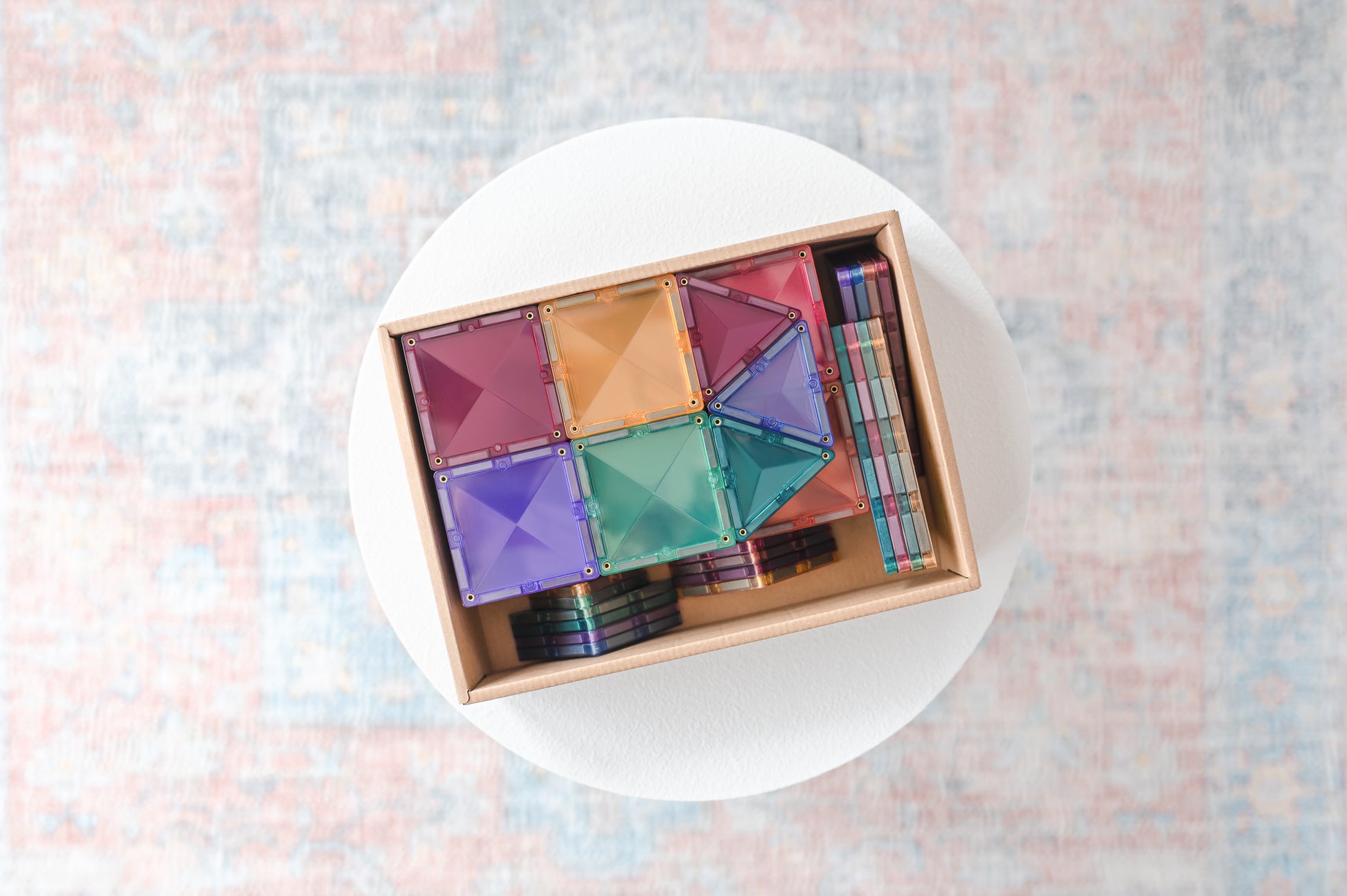 Bovenaanzicht open doos Connetix Pastel Starter Pack 64pc met magnetische bouwstenen op rond tafeltje