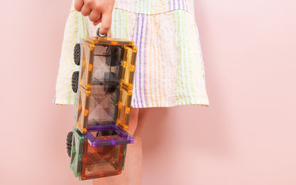 Connetix magnetisch speelgoed pastel wagons vastgehouden door kind in gestreepte jurk roze achtergrond