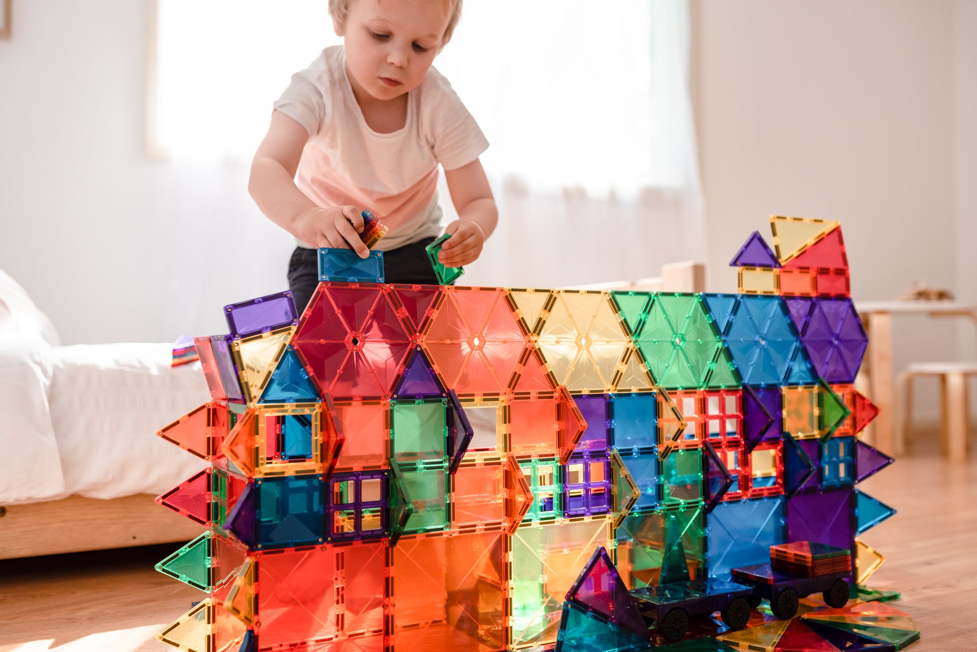 Peuter bouwt grote regenboogstructuur met Connetix Rainbow Mega Pack 212pc magnetische bouwstenen op slaapkamervloer