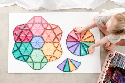 Kind speelt met Connetix pastel magneet tegels en bouwt kleurrijke mandala patronen op speelmat