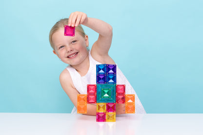 Lachend meisje bouwt figuur met Connetix Bright Portal Pack 48pc magneten speelgoed aan tafel