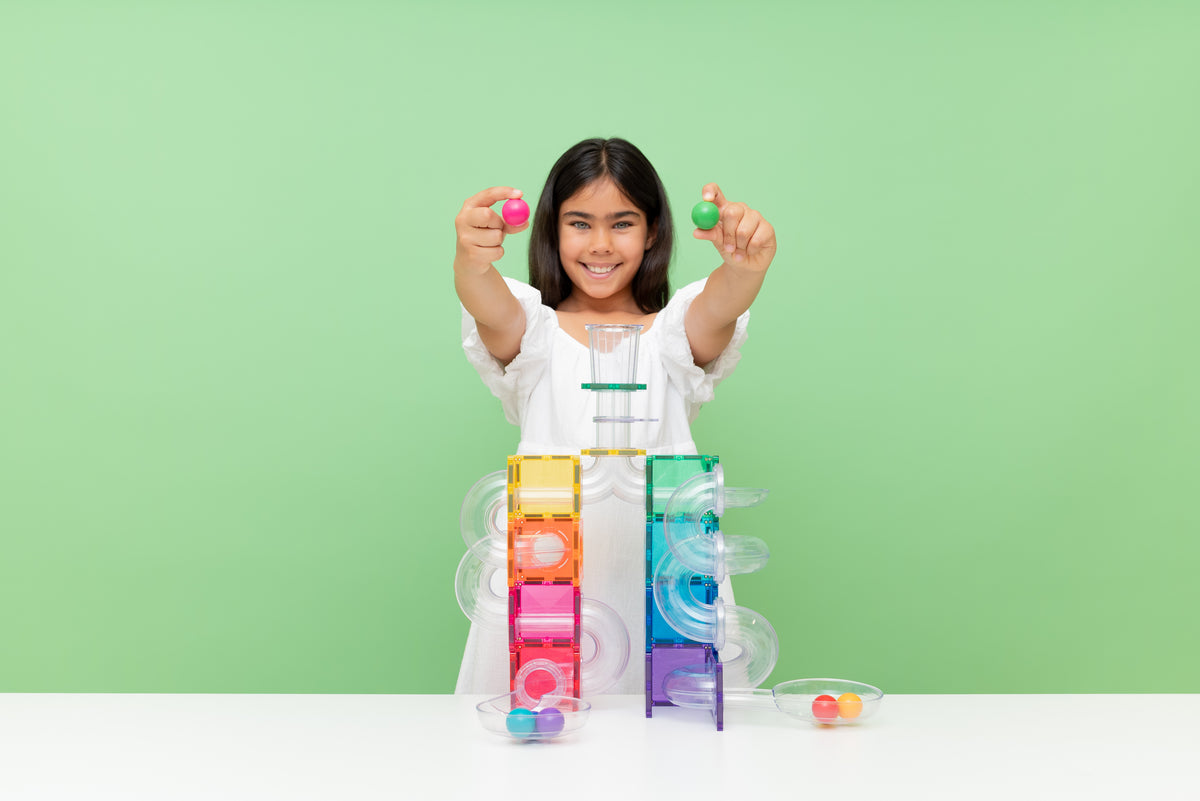 Kind toont Connetix tiles met gekleurde knikkers voor magnetische knikkerbaan constructie op groene achtergrond