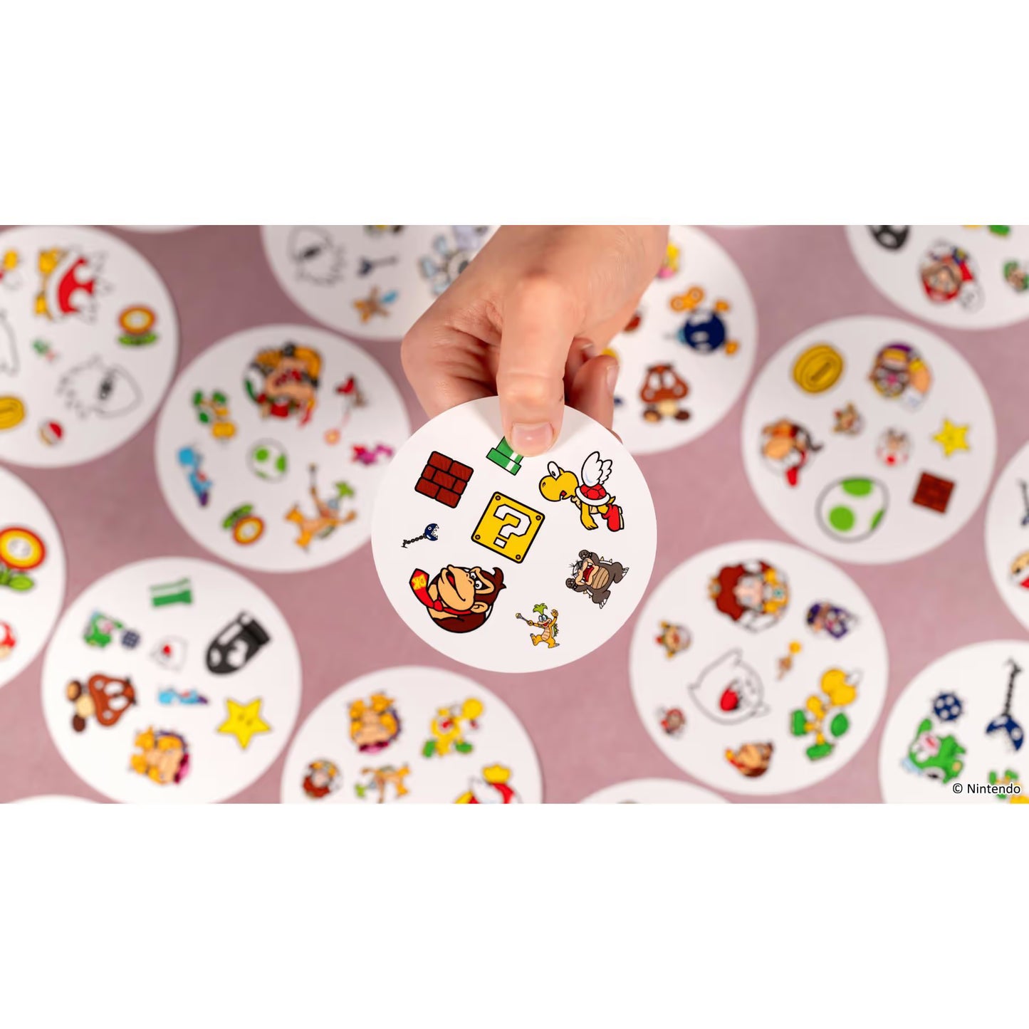 Hand houdt Dobble Super Mario kaart met figuren zoals Donkey Kong en Koopa vast, leuk reactiespel en kaartspel voor het hele gezin.