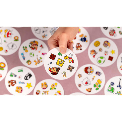 Hand houdt Dobble Super Mario kaart met figuren zoals Donkey Kong en Koopa vast, leuk reactiespel en kaartspel voor het hele gezin.