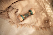 Educatief peuter speelgoed van Jollein: houten rammelaar met blauwe tinten, liggend op een beige hydrofiele doek.