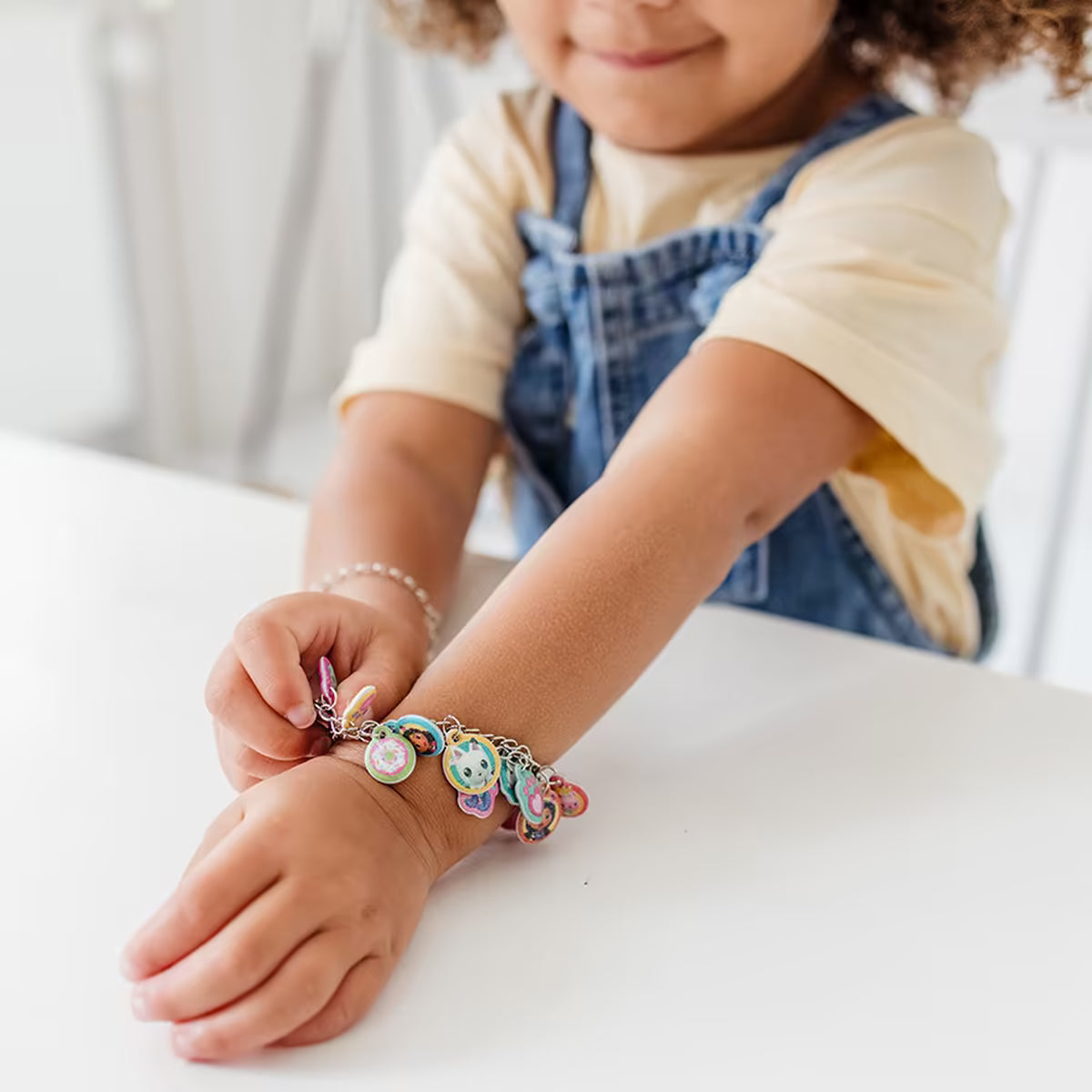 Kind toont Gabby’s Dollhouse armband met kleurrijke bedeltjes om de pols, vrolijk knutsel idee voor jonge kinderen.