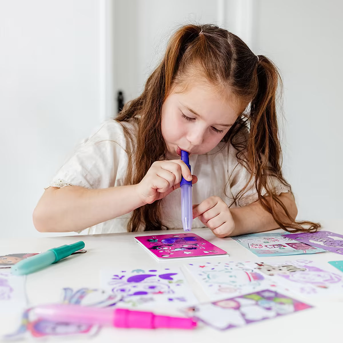 Meisje gebruikt paarse spraypen uit Gabby’s Dollhouse creatieve set om stencil kunstwerk te maken, knutselen met peuters.
