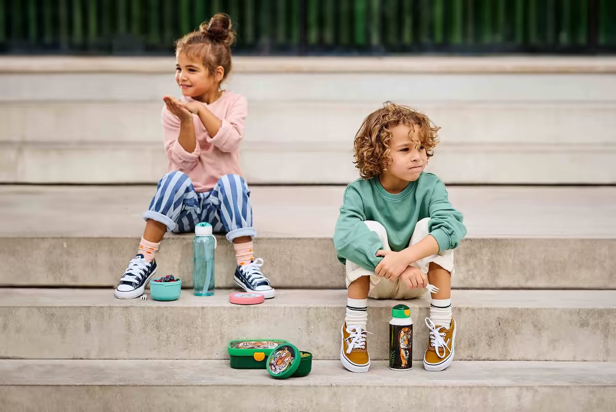 Grote broodtrommel van Mepal voor kinderen, ideaal voor schoollunch, met drinkfles en snackbakje op trap gezeten.