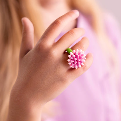 Hey Clay Bijou Rings Flower: meisje draagt roze aster bloemenring van boetseerklei aan haar vinger, paarse achtergrond.