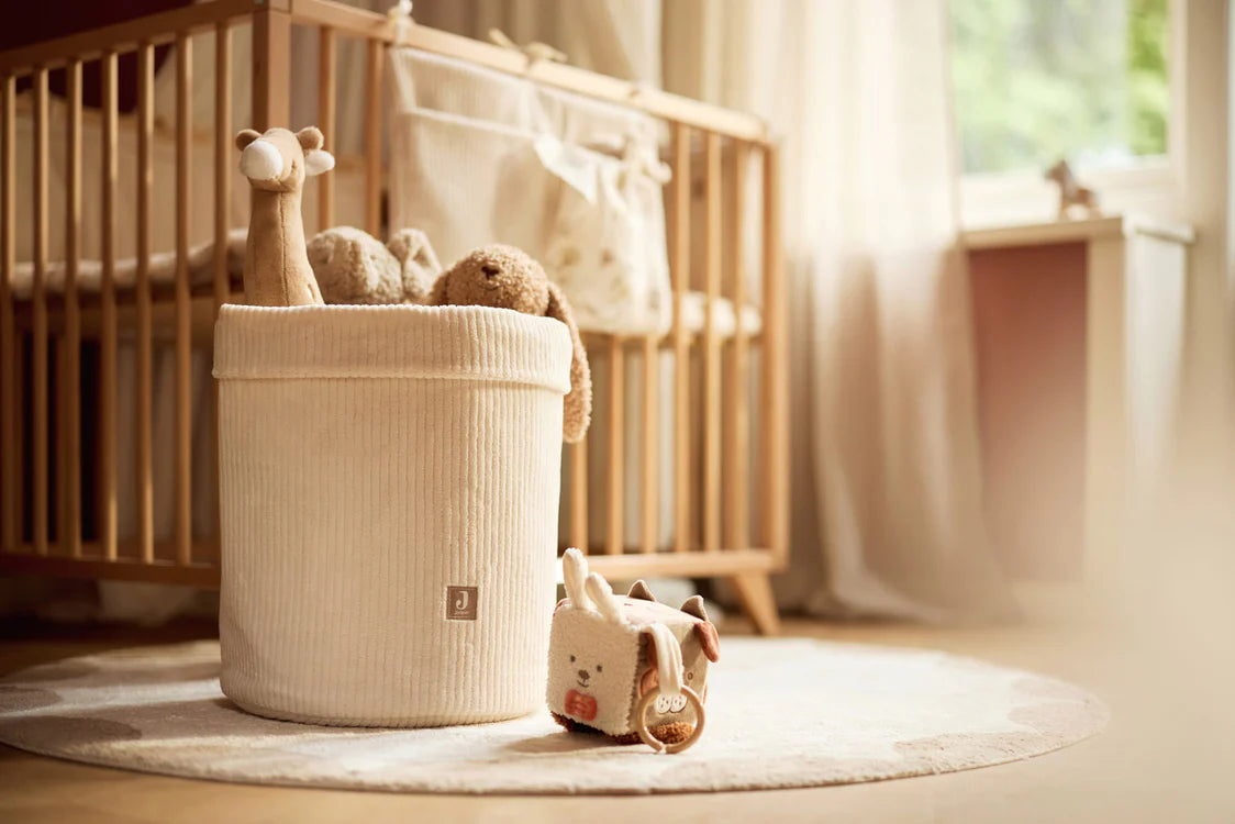 Zachte Jollein activiteitenkubus Animal Friends op vloerkleed in babykamer naast speelgoedmand.