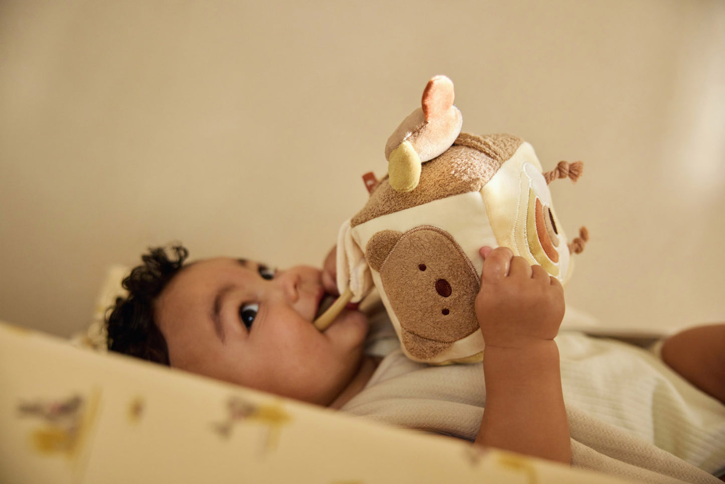 Lachende baby in wieg speelt met Jollein activiteitenkubus koala, educatief speelgoed voor zintuiglijke prikkeling.