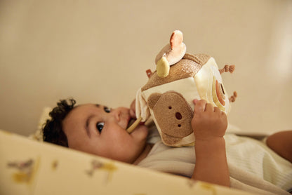 Lachende baby in wieg speelt met Jollein activiteitenkubus koala, educatief speelgoed voor zintuiglijke prikkeling.