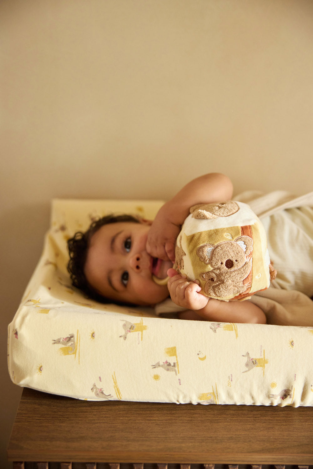 Baby speelt met Jollein sensorisch speelgoed activiteitenkubus op aankleedkussen, koala motief zichtbaar.