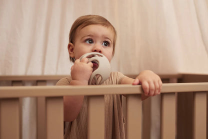 Baby in beige outfit bijt op Jollein bijtring bal in box, flexibel speelgoed in biscuitkleur voor kleintjes.